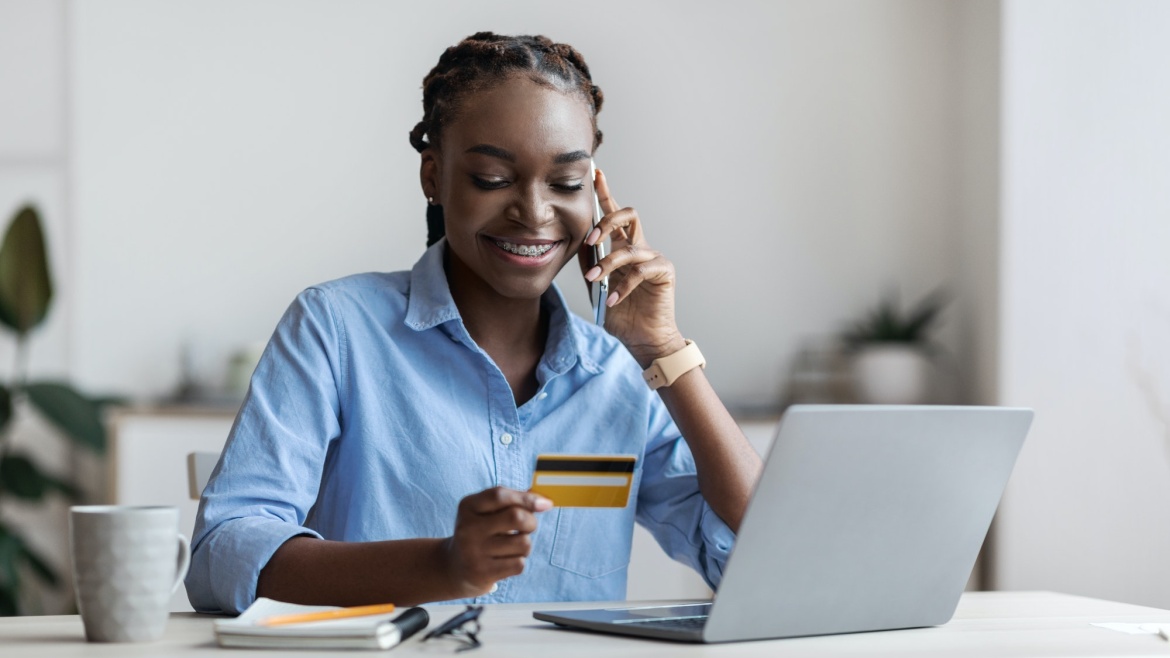 Smiling black female freelancer ordering online with credit card and cellphone